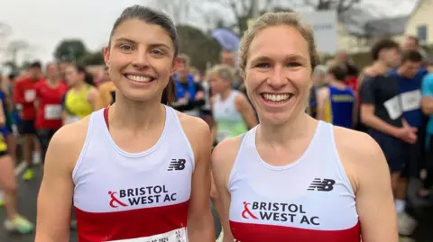 Megan Powell and Jess Heffer stand together smiling looking at the camera wearing Bristol & West AC T-shirts.