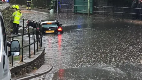 @r00dskins / Twitter A car stuck under the railway bridge in Aberdare