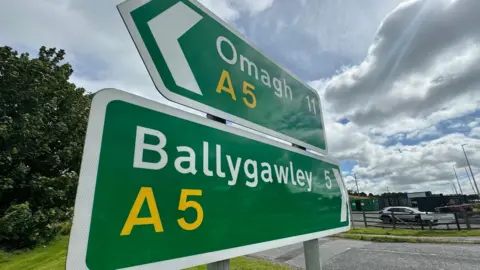 BBC Two green road signs with white writing. One is pointed towards Omagh, the other to Ballygawley