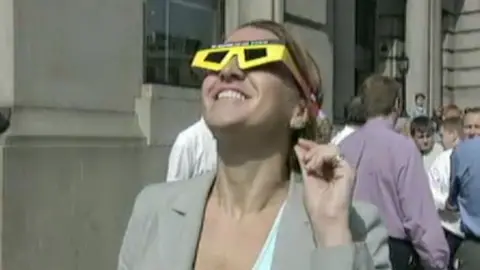Woman in suit jacket wears special glasses for viewing the solar eclipse and looks up at the sky