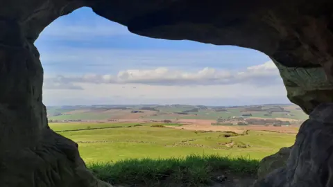 Morven Boyd A view through a gap in stone, showing green fields into the distance. 