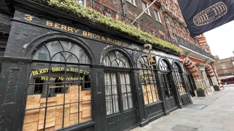An old building in Central London with black mint, gold engraving of Berry Bros & Rudd, and a flag with a wine barrel on it