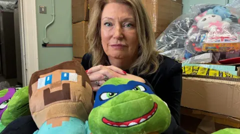 Helen Barnham sits behind counterfeit Minecraft and Ninja Turtle toys with another sack of counterfeit toys bagged up behind her.