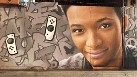 @DoubleA_Charged A mural on a wall in New York City. It is graffiti with the face of Etika, a young male. Beside him are two Nintendo Switch controllers