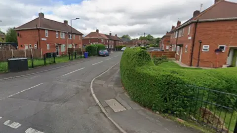 An empty street with red brick houses and large green hedges