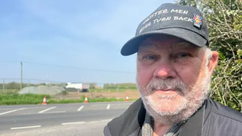 Andrew Turner/BBC Caister Parish Council chairman Kevin Wood near the access to Persimmon Homes' site at Nova Scotia Farm