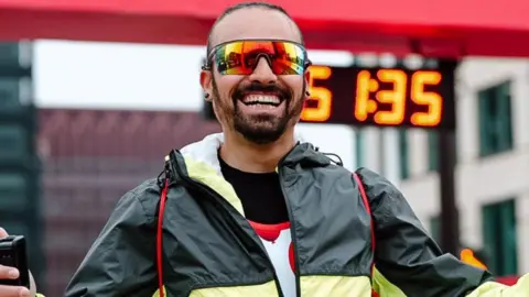 Great Birmingham Run A man dressed in a black and yellow running jacket, sunglasses smiling at the camera