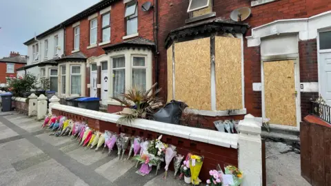 Floral tributes are left outside a boarded-up house in Peter Street, Blackpool