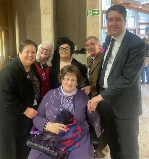 Neil Bibby Marion McMillan, seated in the centre, was in Holyrood to hear the apology along with fellow campaigners and MSPs