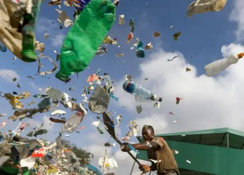 Daniel Irungu/ EPA Man trying to manage flying plastic rubbish.