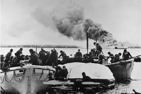 Getty Images Lifeboats carrying crew and soldiers of 1st Battalion Welsh Guards reach shore at Fitzroy, having escaped from the blazing RFA SIR GALAHAD after the devastating Argentine air raid, 8 June 1982