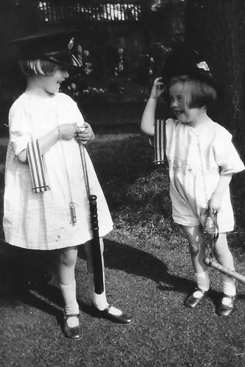 Morganfourman.com Pamela and Hazel Downing, pictured in July 1926. They are wearing light coloured dresses and have police hats on their heads. They are also carrying police whistles, armbands and truncheons. 
