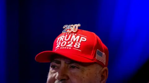Getty Images Man wearing TRUMP 2028 red hat with a '250th' badge on the top in colours of the USA flag
