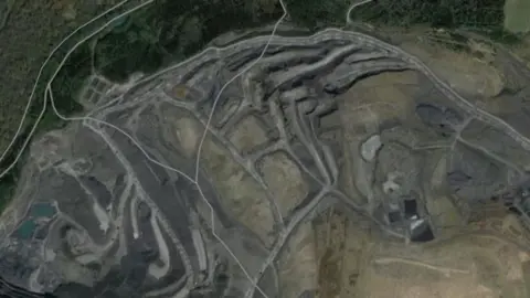 An aerial satellite view of the former Nant Helen opencast mine. In the bottom left are a series of voids filled with water while the rest of the image shows tracks covering the site and ridges where the mining has taken place. 