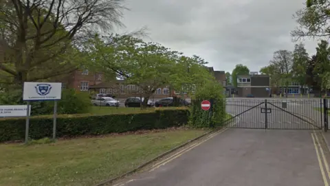 A Google Streetview of the entrance gates to Lutterworth College with a sign stood on grass to the left.