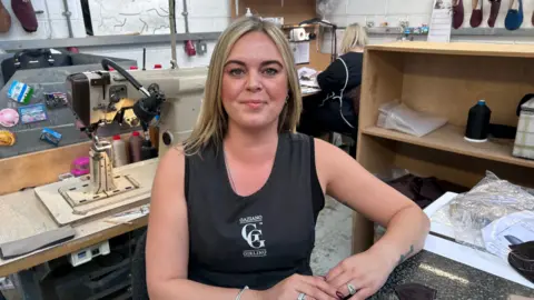 Kate Bradbrook/BBC Chelise Porter looks directly at the camera in a black Gaziano and Girling work vest. She is sitting in a shoe factory