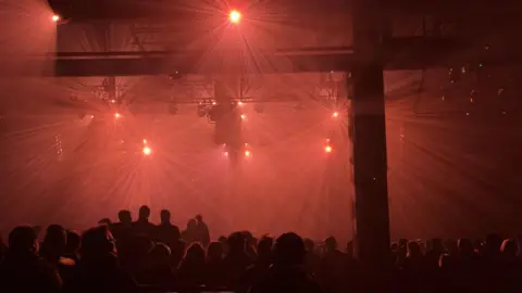 Inside the Prospect Building during the event. The space is dark and lit up by red lights. People are sitting down and silhouetted against the red light.