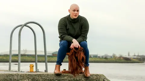 Debbie Burrows Laura sitting on a quay holding her wig