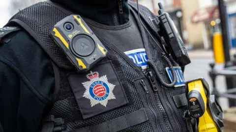 Close-up of police uniform. The black outfit also holds a body camera and a yellow taser gun.