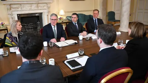 PA Media Sir Keir Starmer speaks at meeting with six other people as they sit around a table in a room at 10 Downing Street.