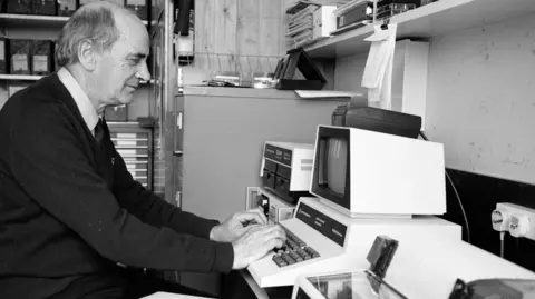 Bangor University Jack Darbyshire sits in front of a computer at Bangor University's School of Ocean Sciences in the 1980s (black and white image)