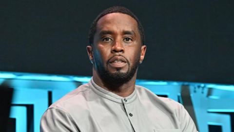 Sean 'Diddy' Combs, looking straight ahead with a neutral expression, sitting in front of a microphone