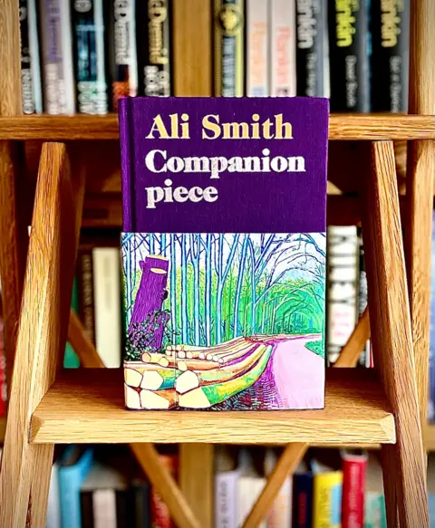X/Nicola Sturgeon A wooden ladder stands in front of a book shelf with a book called 'Companion piece' by Ali Smith on one of its steps. 