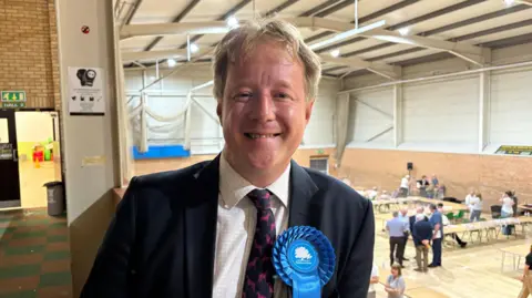 Paul Bristow with a blue rosette on, smiling at the camera