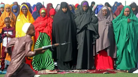 Reuters A boy with a toy gun runs past people praying on Eid in Mogadishu, Somalia - Tuesday 21 August 2018