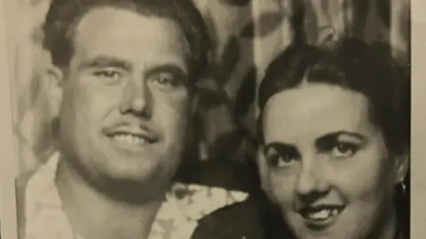 Family handout A black and white image showing Fred in a patterned shirt and jacket after the war, smiling as he looks at the camera next to his wife