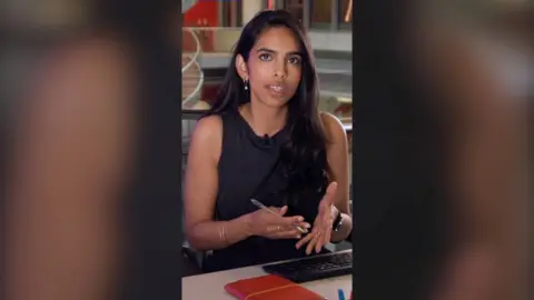 BBC Verify correspondent Merlyn Thomas with long dark hair at an office desk