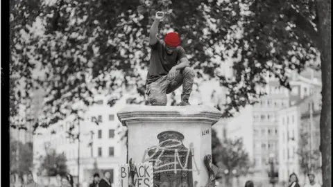 Felix Russell-Saw Manoel Akure standing on the plinth after the statue was pulled down