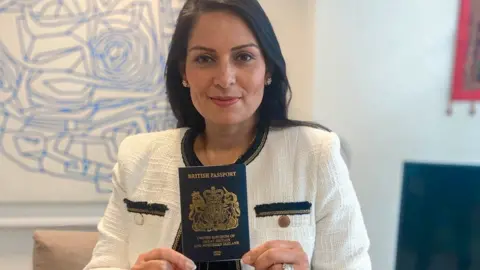 PA Media Home Secretary Priti Patel holding a blue passport