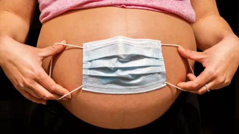 Getty Images Face mask spread over a pregnant woman's stomach