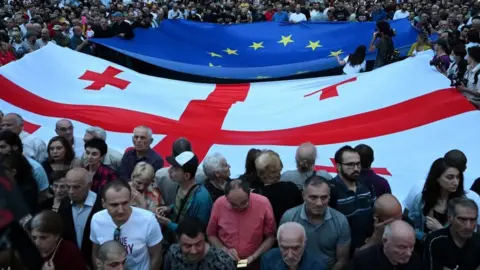 VANO SHLAMOV/AFP Attendees extend a Georgian flag and a EU flag in Tbilisi during a rally gathering tens of thousands of attendees in support of Georgia's candidacy for European Union membership, on June 24, 2022