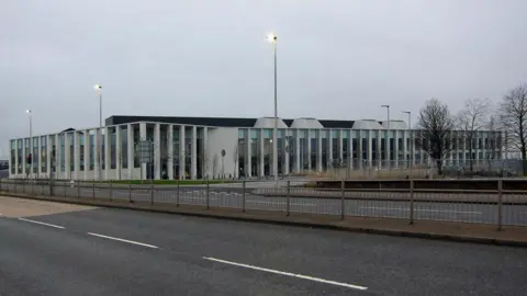 The court building has a series of pillars along its exterior walls. The road normally busy road outside is quite. There are three streetlights switched on.