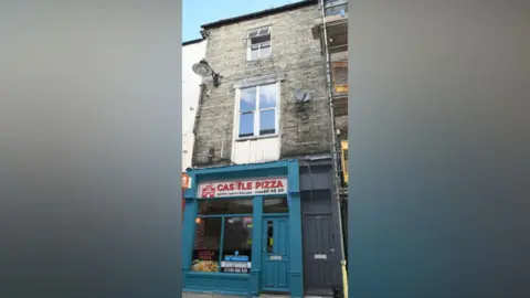 Durham Police A three-storey terraced building where the baby was found. On the ground floor is a pizza shop called Castle Pizza, next to its green frontage is a black door and then two large windows above.
