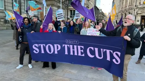 BBC Men and women with banners and flags angry at council cuts gather outside the council's offices