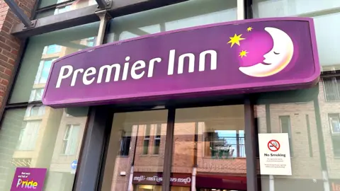 The front facade of a Premier Inn hotel in Bankside, Waterloo, London. The sign is purple with white text and the company logo is to the right of the sign, which is a crescent moon with a sleeping face on it and three stars.