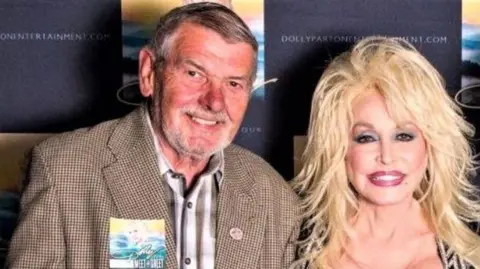 Supplied Rolf Speer and Dolly Parton. They are smiling at the camera. 