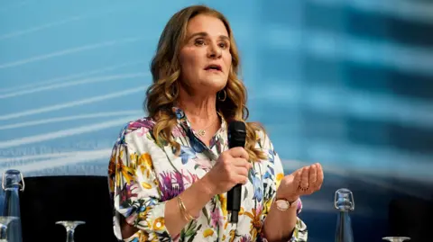 A woman in a floral dress holds a microphone