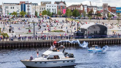 Stockton Council A small white boat passes by as crowds are sat in the amphitheatre. 