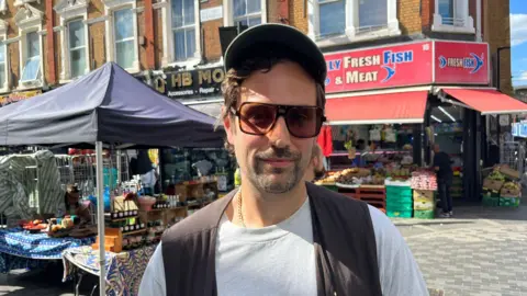 Man in sunglasses and a cap in front of an outdoor market