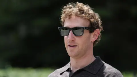 A close-up of Mark Zuckerberg, wearing a set of Meta Ray-Bans and brown top, walking through a park.