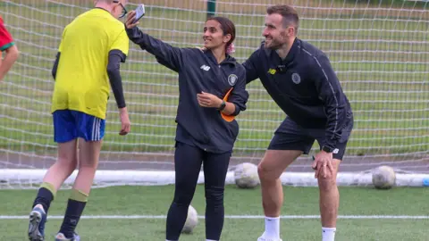 Harrogate Town AFC Sabriah Nawroozi poses for a selfie with a Harrogate Town AFC football player at a training session. She wears black leggings and a black long-sleeved sports top.