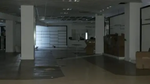 An image of a dimly lit empty department store, with boxes and furniture strewn around the space. 
