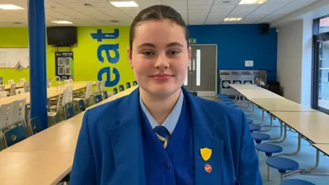 A secondary school student wearing a blue blazer and blue jumper. 