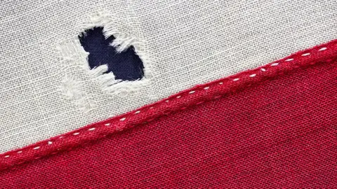 North East Museums Close-up of flag fabric on the white and red section. There is a gunshot tear shown in the white section.