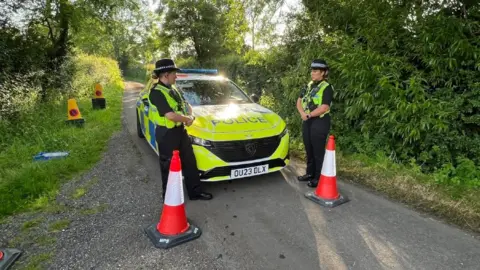 Steve Hubbard/BBC Two police officers stand in front of a police car