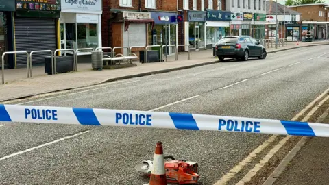 Leicester Media Online Leicestershire Police cordon in place in the day of the scene of an attempted theft of a cash machine from a building society on Sibson Road in Birstall on 6 May 2026. Near the cordon is a traffic cone and an item resembling an angle grinder left on the road.